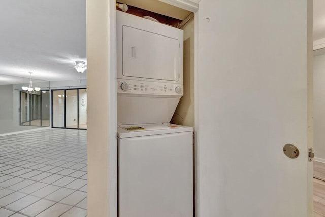 clothes washing area featuring stacked washing maching and dryer, a notable chandelier, and light tile patterned floors