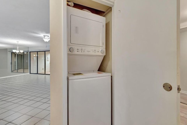 clothes washing area featuring light tile patterned flooring, stacked washer and dryer, and a notable chandelier