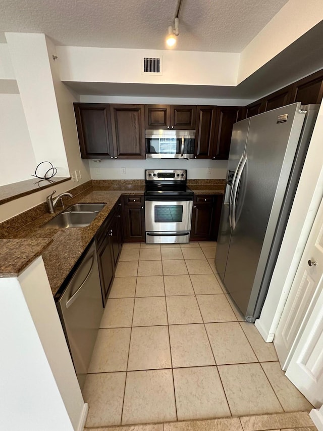 kitchen with stainless steel appliances, a textured ceiling, sink, light tile patterned flooring, and dark brown cabinets