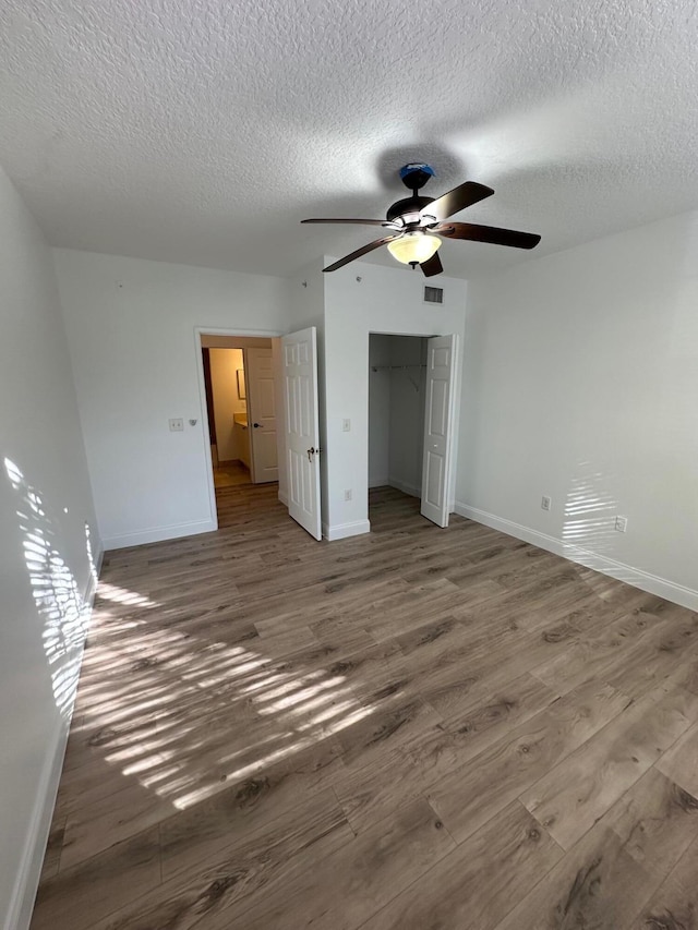 unfurnished bedroom featuring ceiling fan, wood-type flooring, a textured ceiling, and a closet