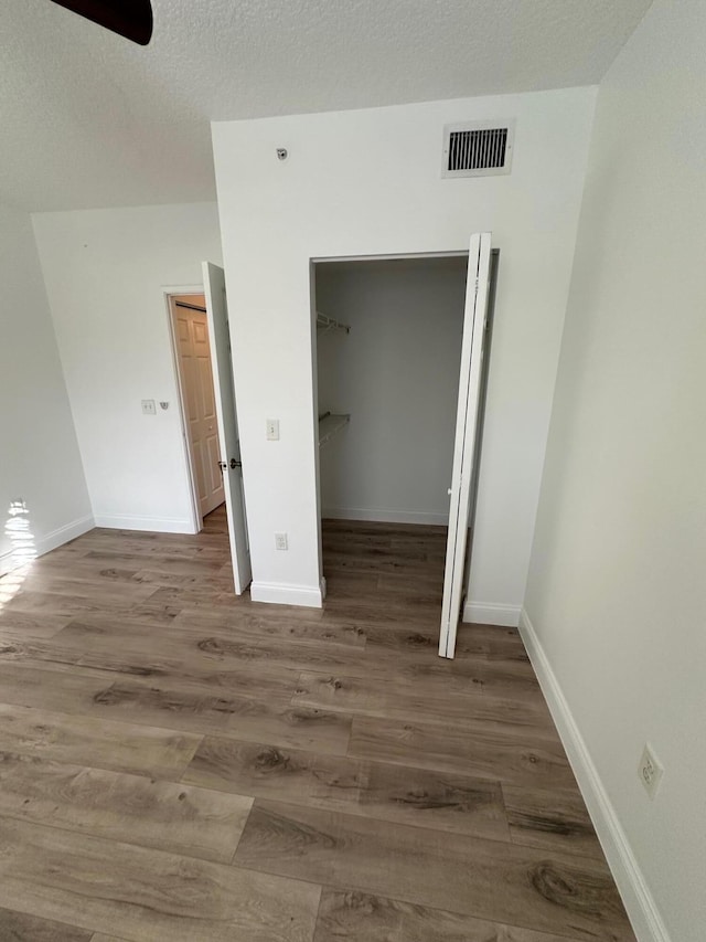 unfurnished bedroom with a closet, a spacious closet, a textured ceiling, dark hardwood / wood-style floors, and ceiling fan