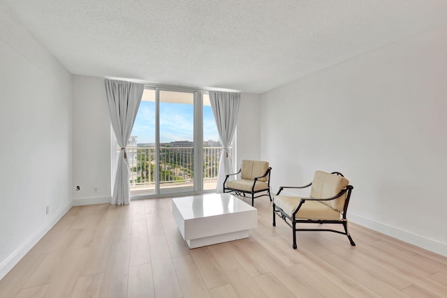 living area featuring a textured ceiling, a wall of windows, and light hardwood / wood-style flooring