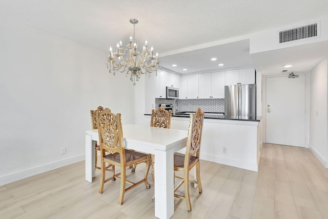 dining space with baseboards, visible vents, an inviting chandelier, a textured ceiling, and light wood-style floors