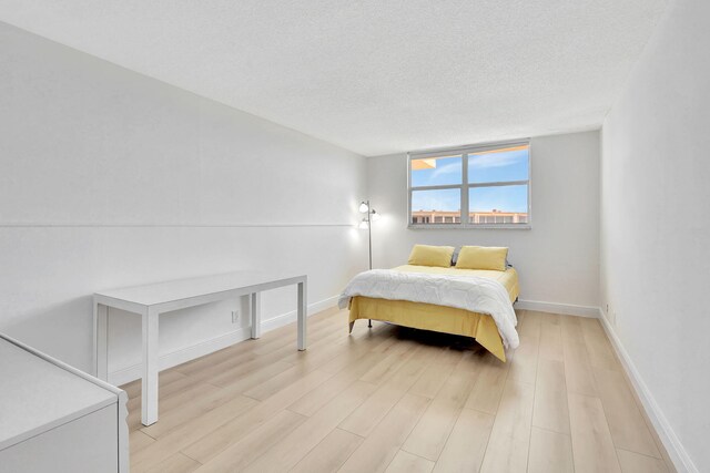 bedroom with a textured ceiling, light wood-style floors, and baseboards