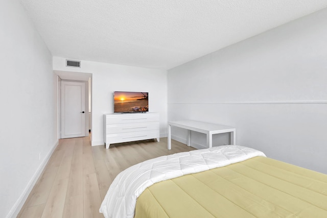 bedroom featuring a textured ceiling, visible vents, baseboards, and light wood-style floors