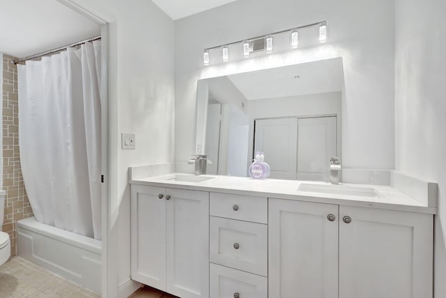 bathroom with toilet, double vanity, a sink, and shower / bath combo