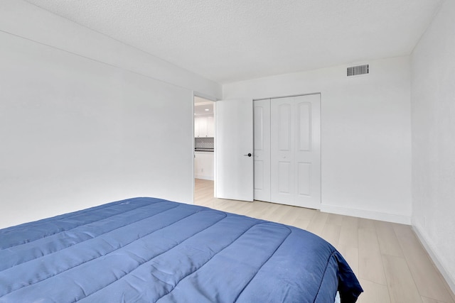 bedroom with a closet, visible vents, light wood-style flooring, a textured ceiling, and baseboards