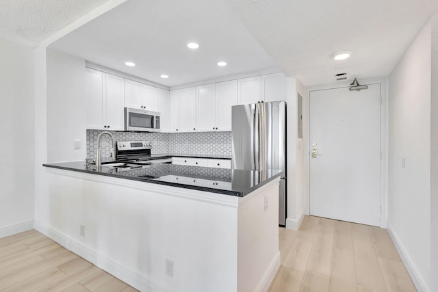 kitchen with appliances with stainless steel finishes, dark countertops, backsplash, and a peninsula