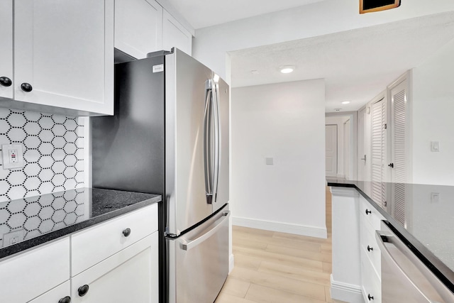 kitchen with white cabinets, stainless steel appliances, dark stone countertops, tasteful backsplash, and light wood-type flooring