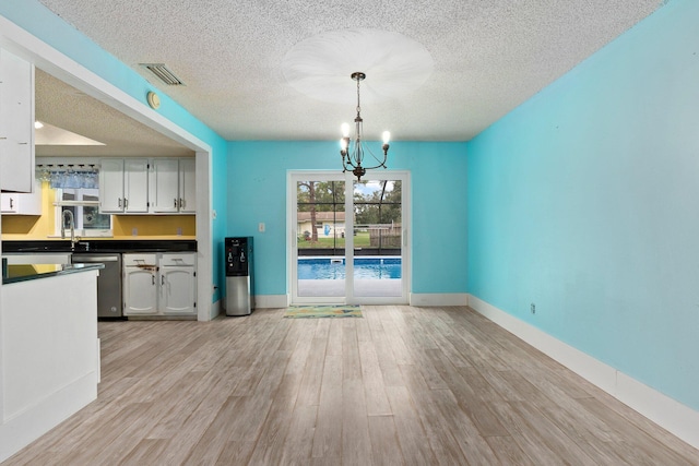 unfurnished dining area featuring light wood-type flooring, a textured ceiling, a chandelier, and sink