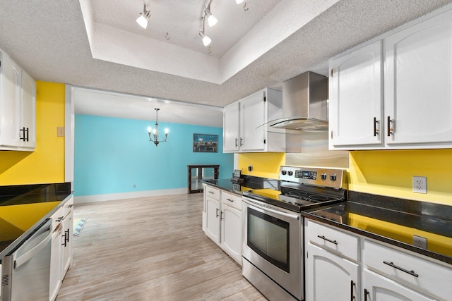 kitchen featuring stainless steel appliances, a textured ceiling, wall chimney range hood, white cabinetry, and decorative light fixtures