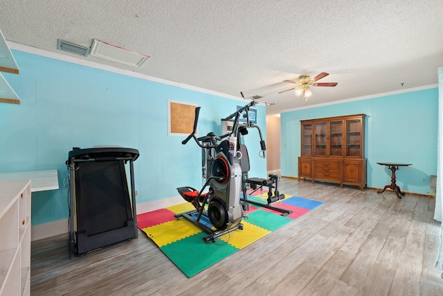 exercise area featuring ornamental molding, wood-type flooring, ceiling fan, and a textured ceiling