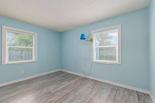 empty room with light wood-type flooring and a textured ceiling