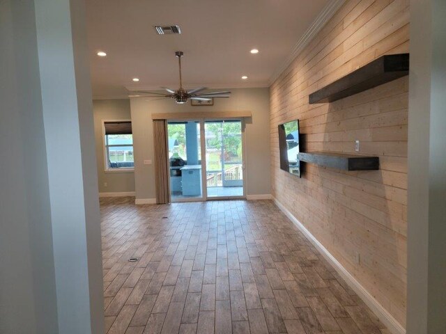 empty room featuring wood finished floors, baseboards, visible vents, ceiling fan, and ornamental molding