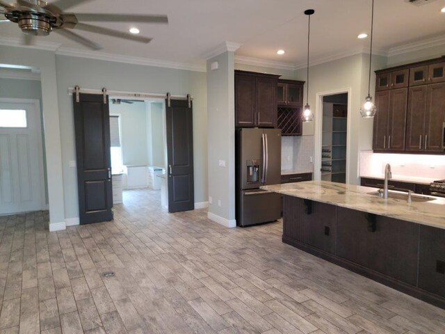 kitchen featuring light wood finished floors, a sink, dark brown cabinetry, a barn door, and stainless steel fridge