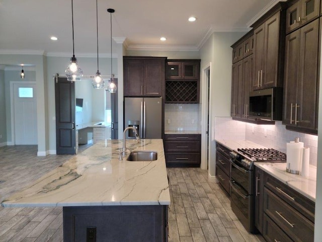 kitchen with a barn door, appliances with stainless steel finishes, light wood-style floors, and a sink