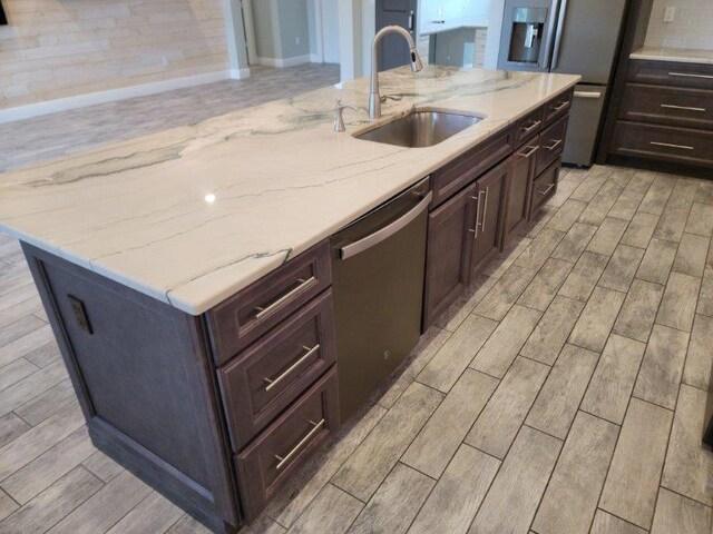 kitchen featuring light stone countertops, wood tiled floor, a sink, stainless steel appliances, and dark brown cabinets