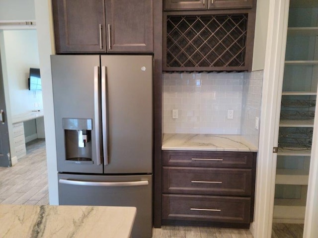 kitchen featuring dark brown cabinetry, stainless steel fridge, and light stone countertops