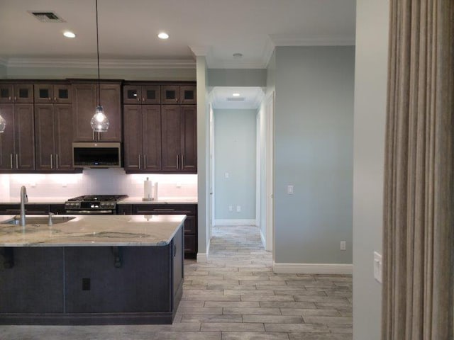 kitchen featuring dark brown cabinets, backsplash, light stone countertops, appliances with stainless steel finishes, and a sink