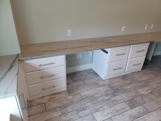 interior space with light stone counters, built in desk, and white cabinets