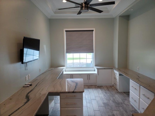 unfurnished office with light wood finished floors, built in desk, crown molding, and a ceiling fan