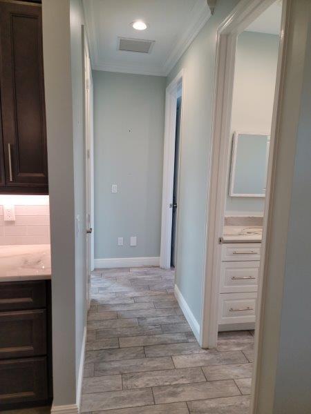 hallway with visible vents, baseboards, crown molding, and wood finish floors