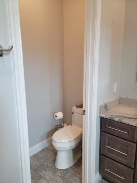 bathroom featuring baseboards, toilet, wood finished floors, and vanity