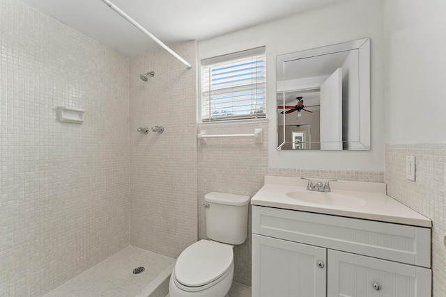 bathroom with a tile shower, ceiling fan, toilet, vanity, and tile walls