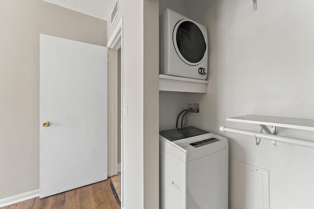 laundry area with a textured ceiling, light wood-type flooring, and stacked washer and dryer