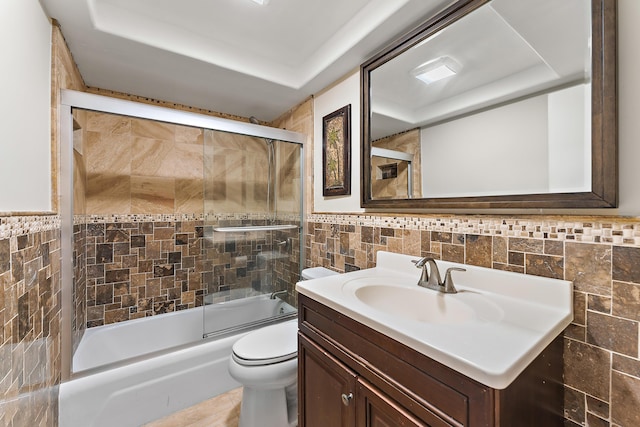 full bathroom featuring vanity, toilet, combined bath / shower with glass door, and tile walls