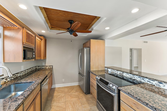 kitchen with ceiling fan, sink, stainless steel appliances, a raised ceiling, and dark stone countertops