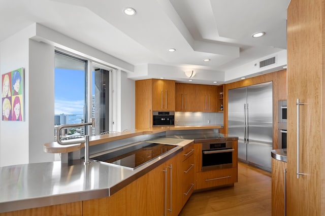 kitchen featuring stainless steel appliances, stainless steel counters, backsplash, and light wood-type flooring