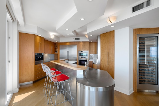 kitchen with a breakfast bar, sink, tasteful backsplash, light hardwood / wood-style flooring, and stainless steel appliances