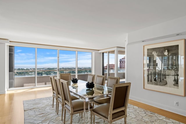 dining space with a water view, expansive windows, and light wood-type flooring