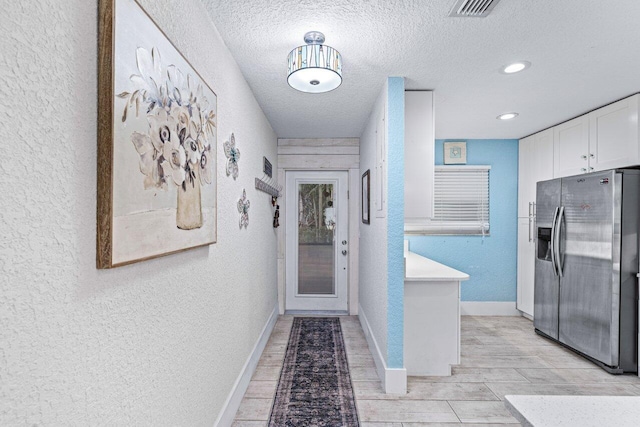 hall with a textured ceiling and light wood-type flooring