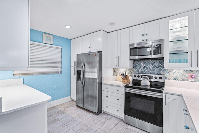 kitchen featuring white cabinets, backsplash, appliances with stainless steel finishes, and light hardwood / wood-style flooring