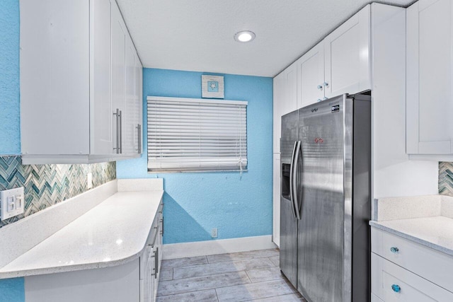 kitchen featuring white cabinets, stainless steel fridge with ice dispenser, backsplash, and light stone counters