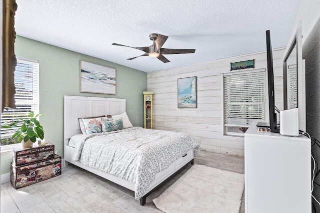 bedroom featuring a textured ceiling, ceiling fan, and wood walls