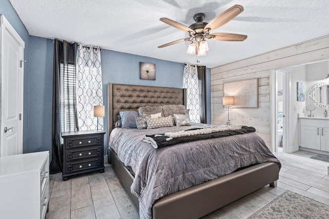 bedroom featuring ceiling fan, light wood-type flooring, wooden walls, and connected bathroom