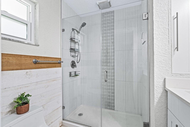 bathroom with vanity, wood walls, toilet, a textured ceiling, and walk in shower