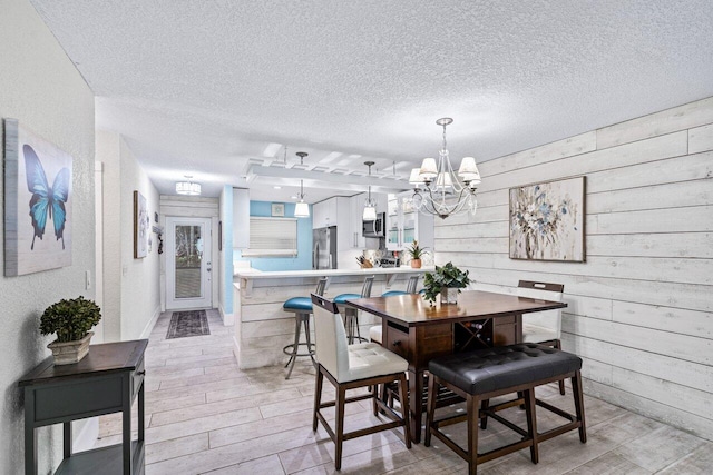 dining space featuring wood walls, light hardwood / wood-style floors, a textured ceiling, and a notable chandelier