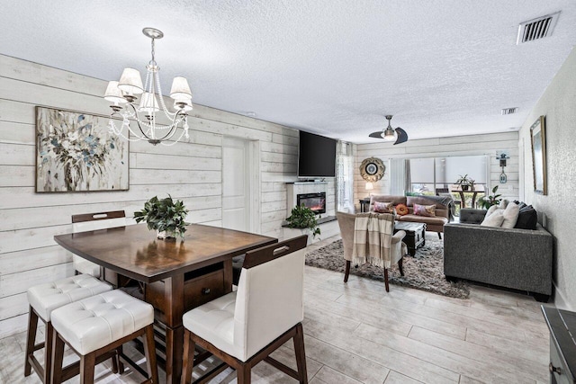 dining area with wood walls, light wood-type flooring, a textured ceiling, and a chandelier