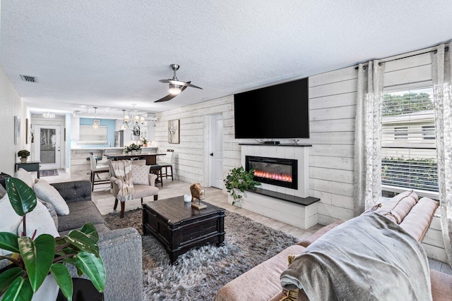 living room featuring ceiling fan, wood walls, and a textured ceiling