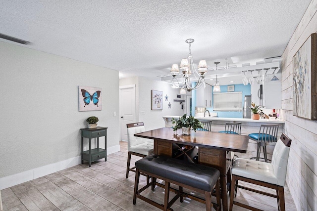 dining area with light wood-type flooring, a textured ceiling, and a notable chandelier