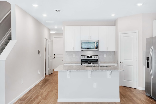 kitchen with a breakfast bar area, light stone counters, white cabinetry, a center island with sink, and appliances with stainless steel finishes