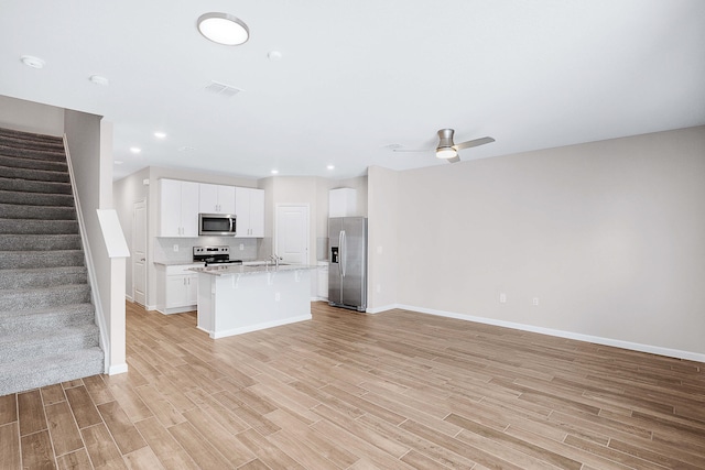 kitchen with light stone counters, light hardwood / wood-style flooring, appliances with stainless steel finishes, a kitchen island with sink, and white cabinets