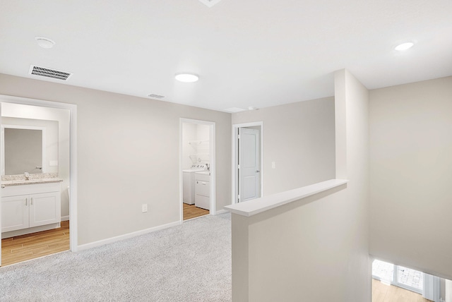 hallway with light carpet, sink, and washing machine and clothes dryer