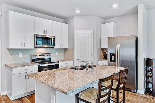 kitchen with stainless steel appliances, light hardwood / wood-style flooring, a center island with sink, and sink