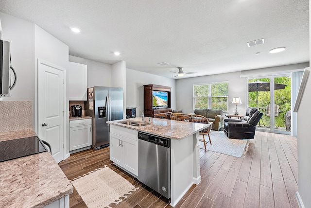 kitchen with sink, a center island with sink, appliances with stainless steel finishes, light stone countertops, and white cabinets