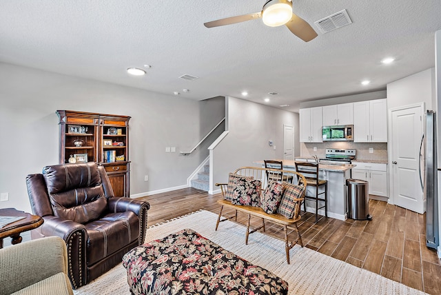 living room featuring dark wood-type flooring, a textured ceiling, and ceiling fan